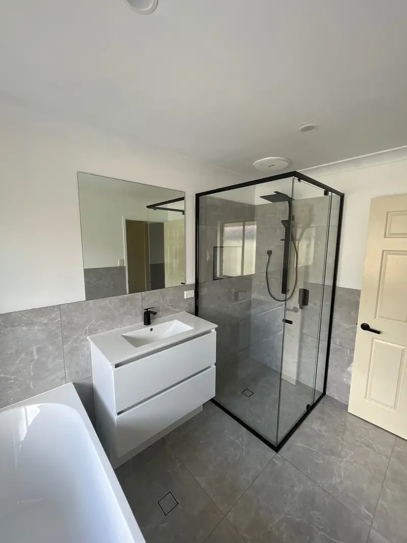 Black semi-frameless shower screen beside a white vanity