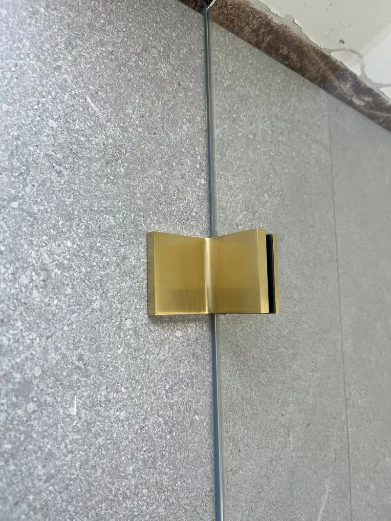 Brushed brass shower hinge against stone-look tiles