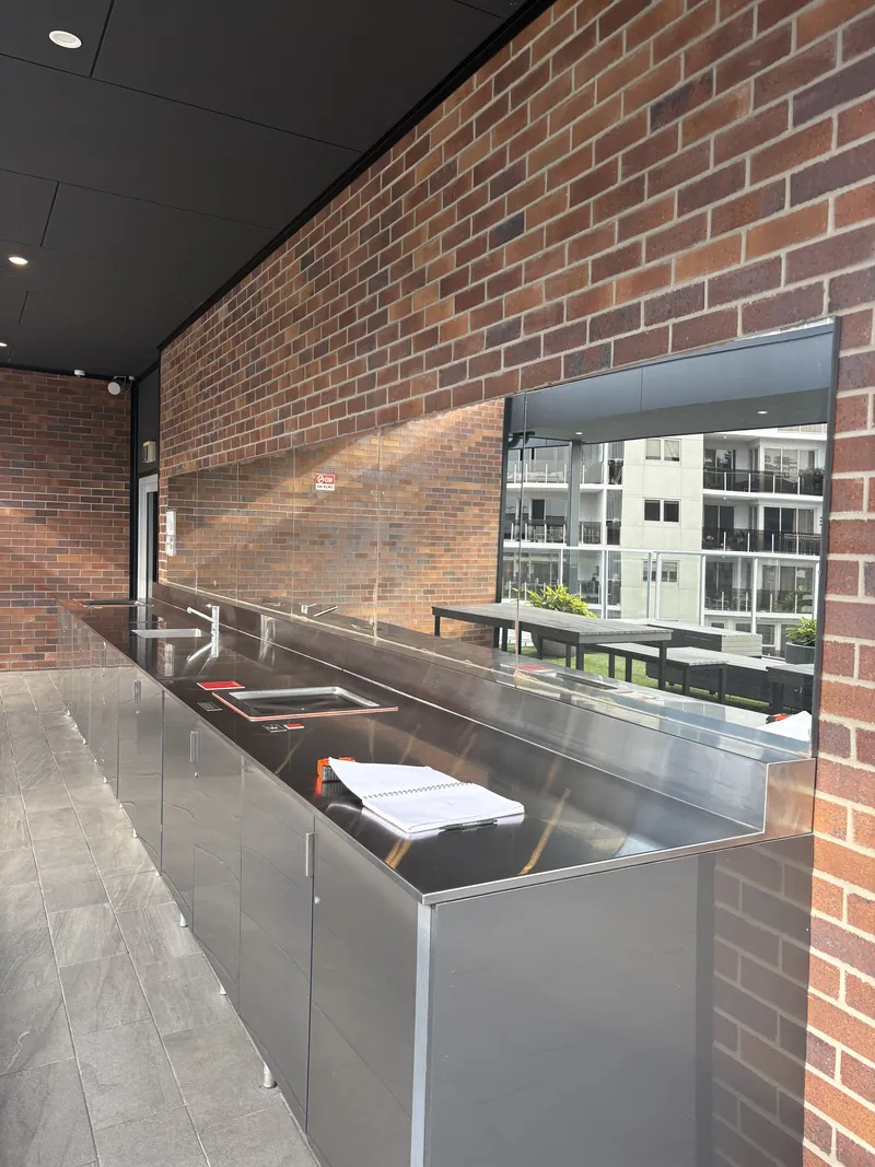 Long commercial mirror splashback in a rooftop outdoor BBQ kitchen with brick wall, Brisbane