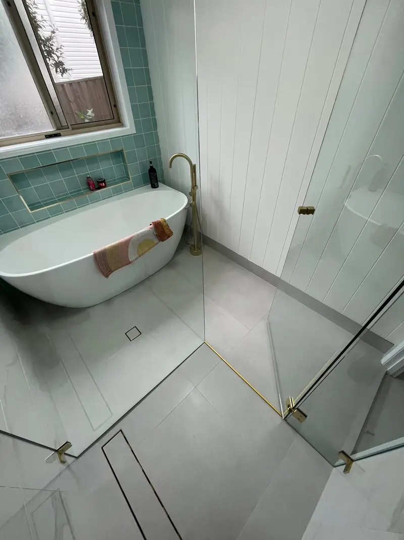 Frameless shower screen with brushed brass hardware beside a freestanding bath in a Brisbane bathroom