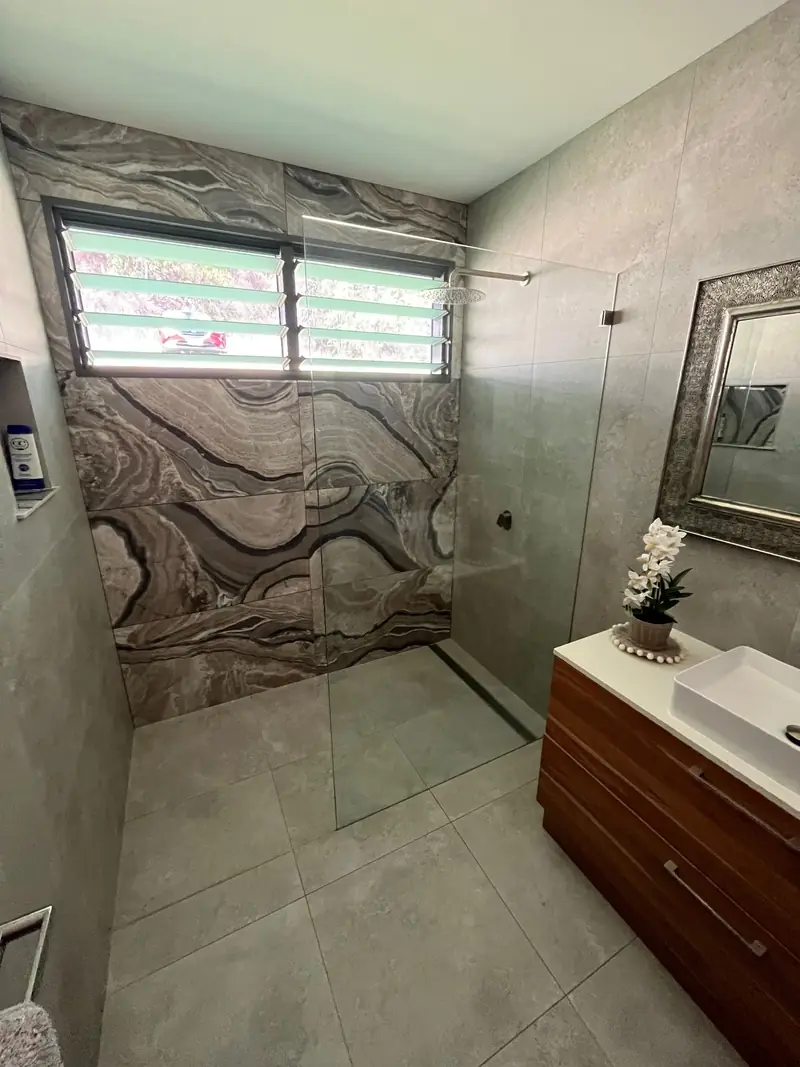 Frameless shower screen in a bathroom with a marble feature wall