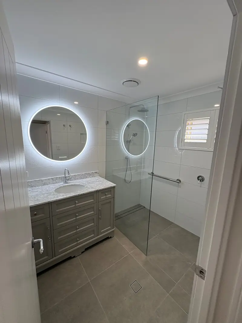 Frameless shower screen beside a round mirror
