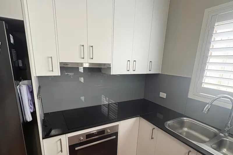 Grey back-painted glass kitchen splashback with white cabinets, Brisbane