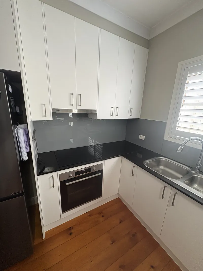 Grey glass kitchen splashback with white cabinets and black benchtop, Brisbane