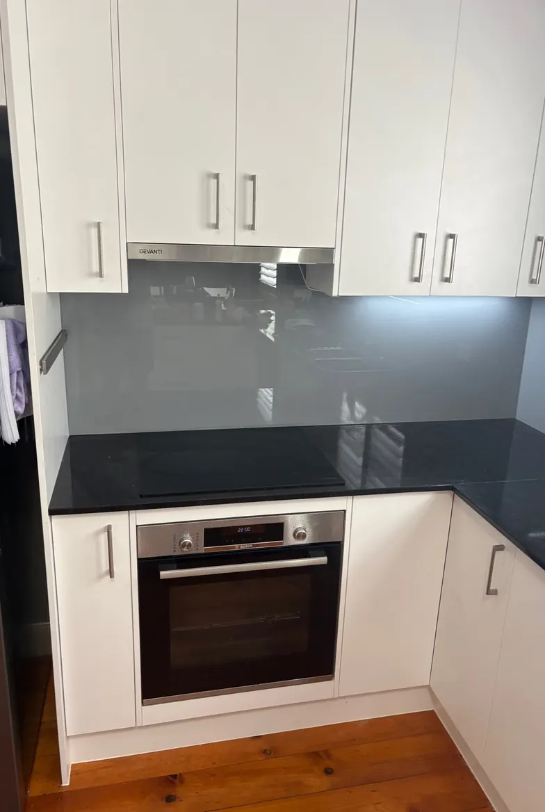 Grey glass kitchen splashback above a black benchtop and oven, Brisbane home