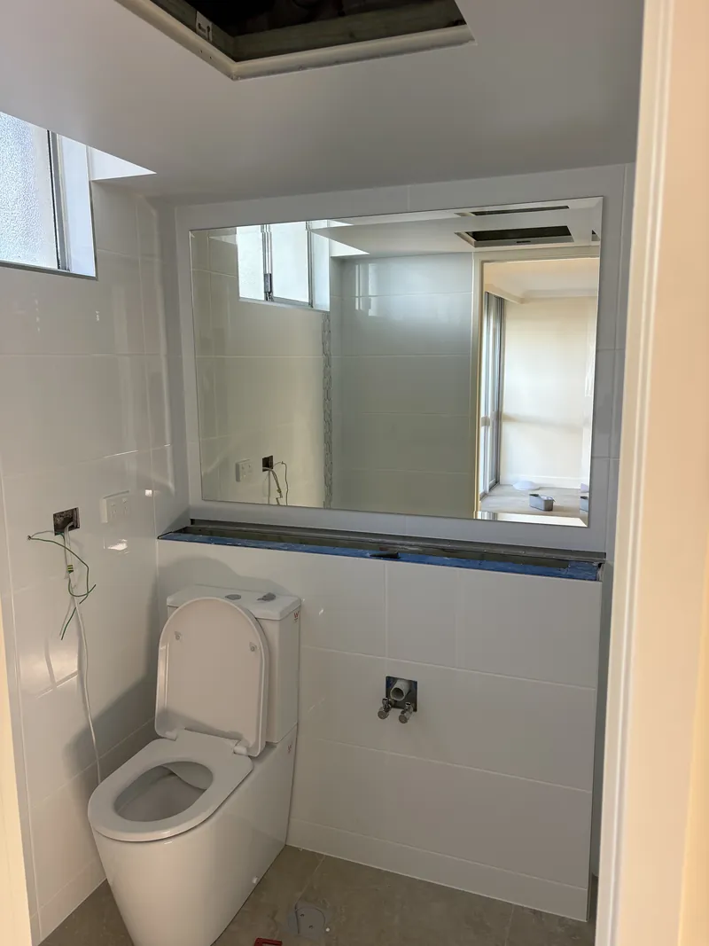 Large frameless bevelled-edge wall mirror above a vanity ledge in a white-tiled bathroom, Brisbane