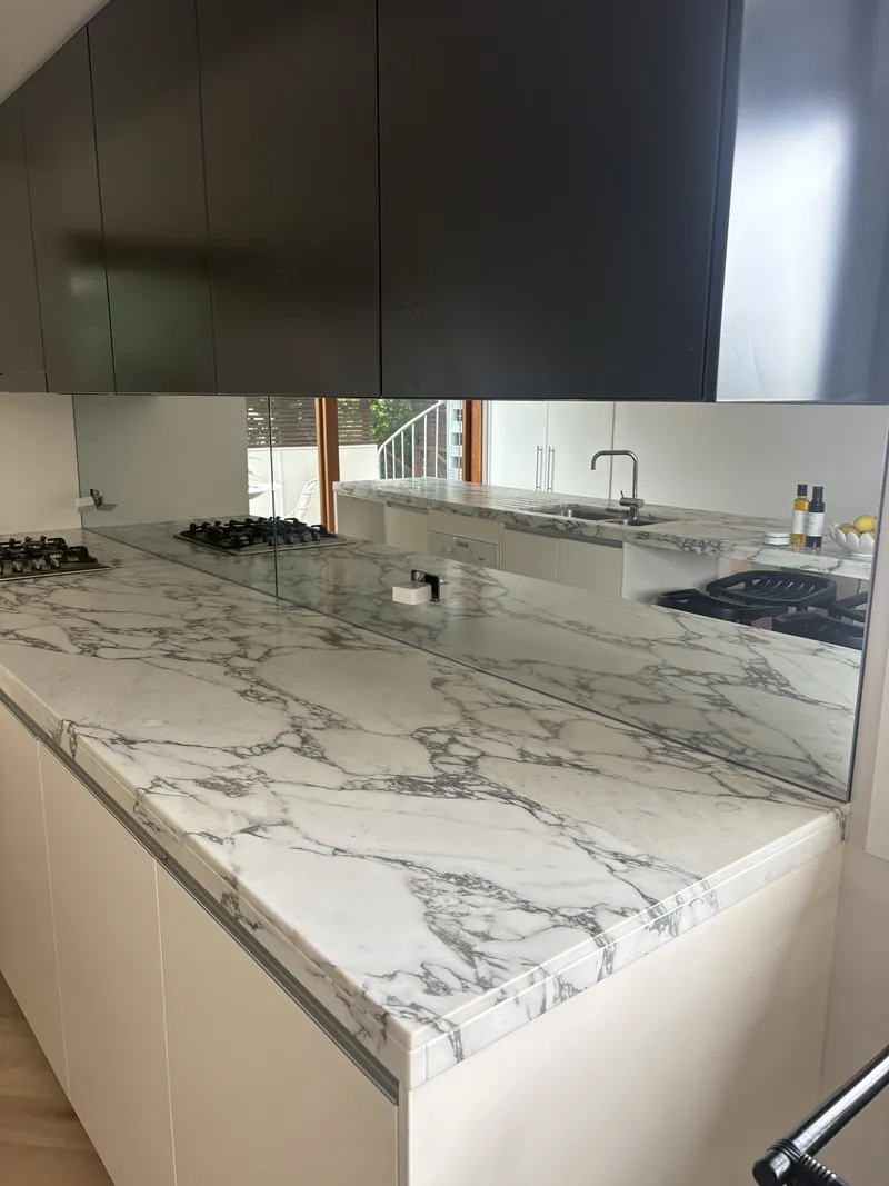 Mirror glass kitchen splashback with marble benchtop and black overhead cabinets, Brisbane