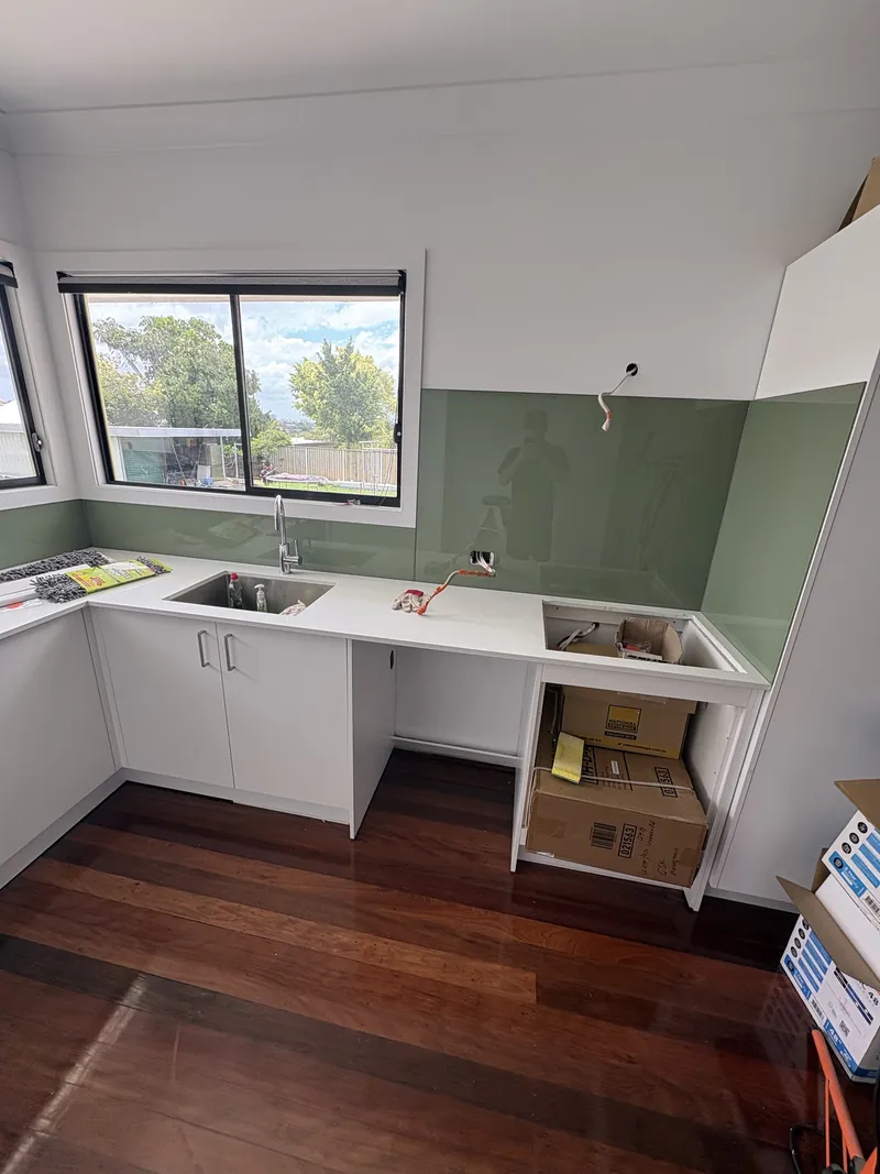 Sage green glass splashback under a window in a kitchen laundry, Brisbane