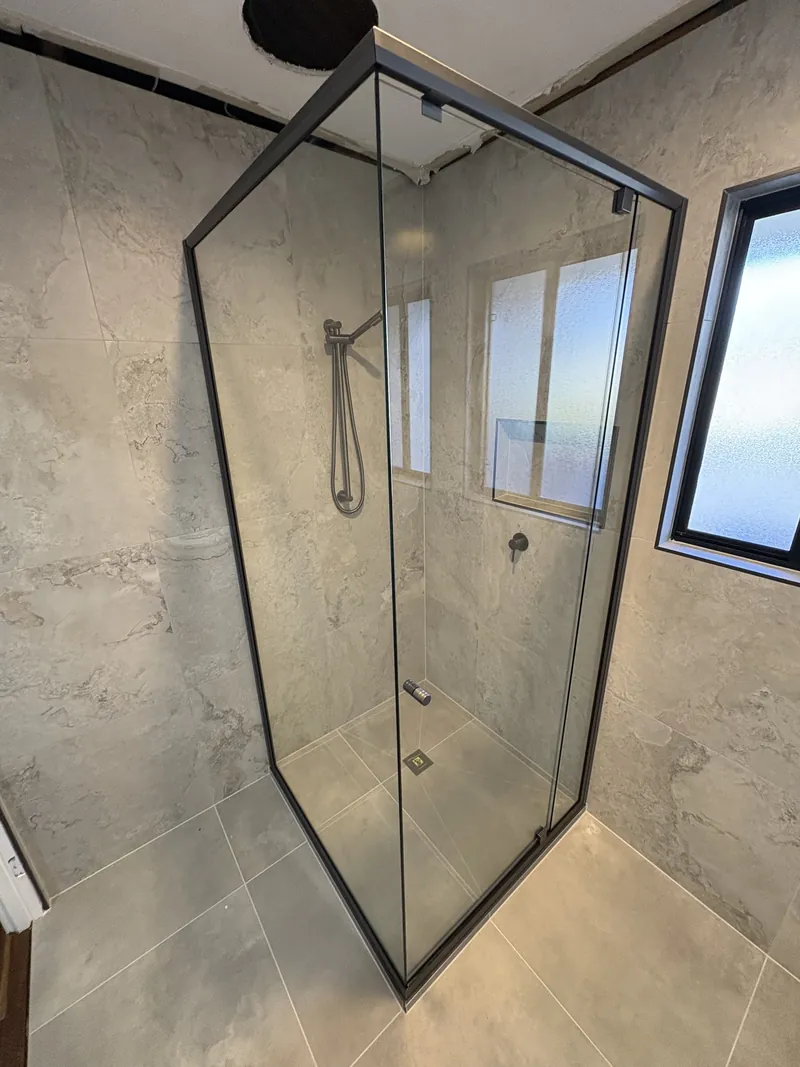Semi-frameless corner shower with matte black frame and stone-look tiles, Brisbane