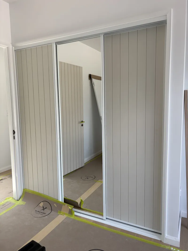 Three-panel sliding wardrobe doors with VJ-panel inserts and centre mirror in a white frame, Brisbane